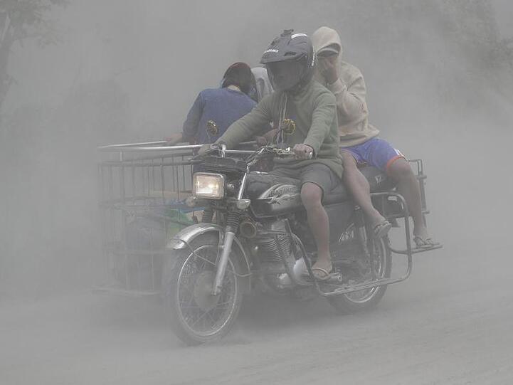 Eine Familie fährt in der Provinz Cavite auf einem Motorrad durch eine Aschewolke.