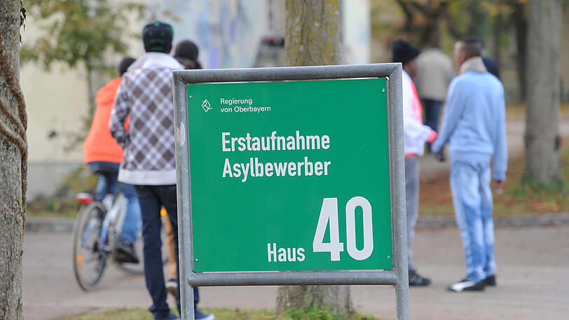 Flüchtlinge halten sich in der Erstaufnahmeeinrichtung für Asylbewerber auf dem Gelände der Bayernkaserne im Freien hinter einem Schild auf.