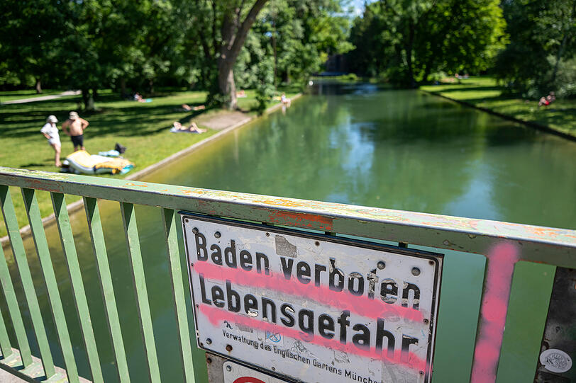 Ein Schild mit der Aufschrift "Baden verboten – Lebensgefahr – Verwaltung des Englischen Garten München" hängt an einem Brückengelände über dem Eisbach im Englischen Garten. Ein Schild mit der Aufschrift "Baden verboten – Lebensgefahr – Verwaltung des Englischen Garten München" hängt an einem Brückengelände über dem Eisbach im Englischen Garten.