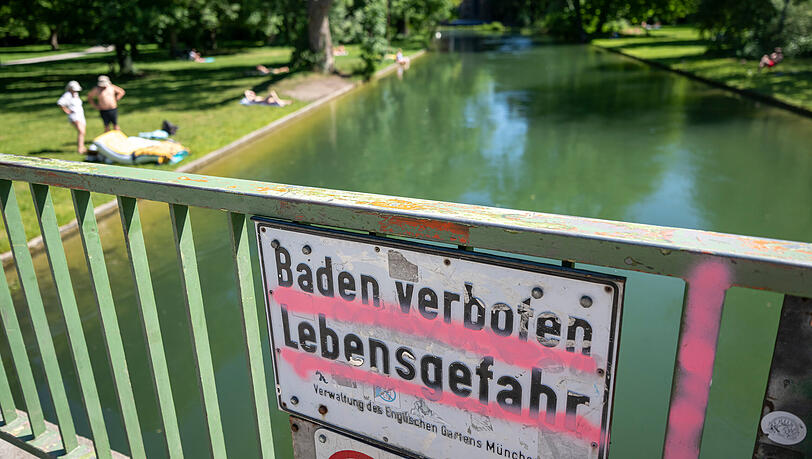 Ein Schild mit der Aufschrift "Baden verboten &ndash; Lebensgefahr &ndash; Verwaltung des Englischen Garten M&uuml;nchen" h&auml;ngt an einem Br&uuml;ckengel&auml;nde &uuml;ber dem Eisbach im Englischen Garten.
