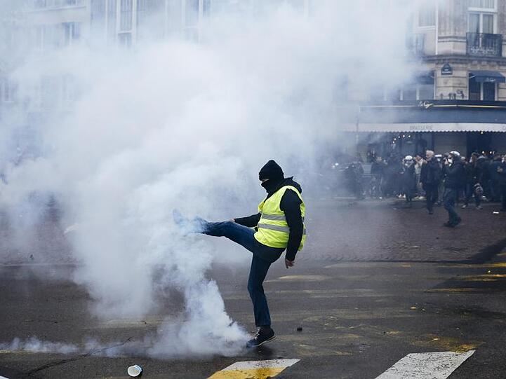 Ein Demonstrant tritt einen Tränengasbehälter von sich weg.