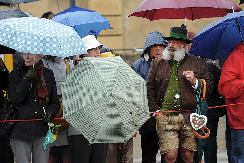 Die Zuschauer lassen sich vom Wetter nicht abhalten und beobachten den Zug am Straßenrand - gut geschützt von ihren Regenschirmen.
