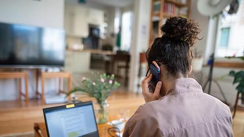 Eine Frau nimmt aus ihrem Wohnzimmer an einer Telefonkonferenz teil. Foto: Sebastian Gollnow/dpa
