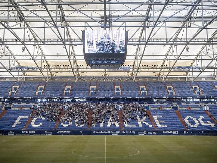 Trauernde Schalke-Fans verfolgen auf dem Videowürfel in der Arena die Gedenkfeier.