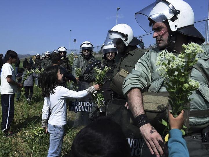 Kinder von Migranten bieten Bereitschaftspolizisten Blumen am Zaun eines Flüchtlingslagers an.