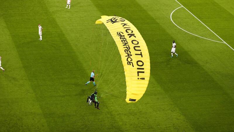 Ein Greenpeace-Aktivist landet mit einem Motorschirm-Flieger bei einer Protestaktion auf dem Spielfeld.