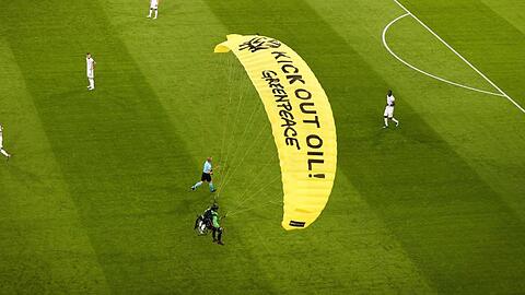 Ein Greenpeace-Aktivist landet mit einem Motorschirm-Flieger bei einer Protestaktion auf dem Spielfeld.