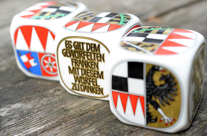 Drei Porzellan-Frankenwürfel, auf denen neben dem Schriftzug «Es gilt dem gewürfelten Franken mit diesem Würfel zu danken» die Wappen der fränkischen Regierungsbezirke aufgebracht sind