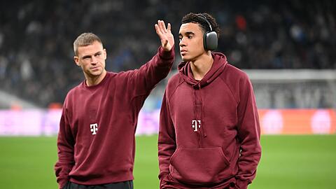 Bayerns Joshua Kimmich (l) und Jamal Musiala gehen vor dem Spiel über den Platz.