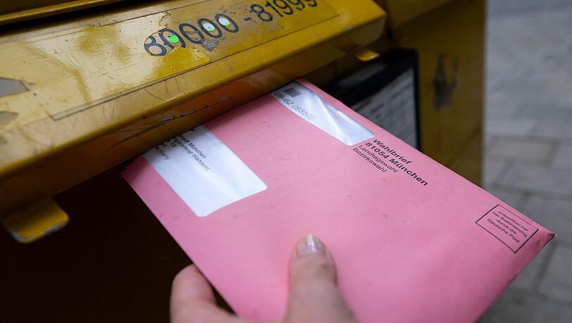 Eine Frau wirft einen Wahlbrief für die Landtags- und Bezirkswahlen in einen Briefkasten.