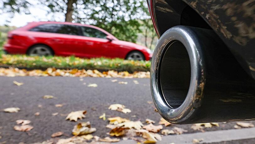 Hinter dem Auspuff eines Pkw fährt ein Auto vorbei.