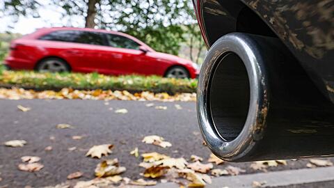 Hinter dem Auspuff eines Pkw fährt ein Auto vorbei.