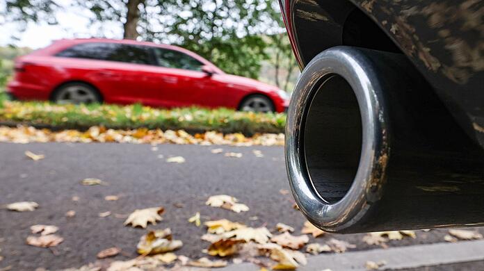 Hinter dem Auspuff eines Pkw fährt ein Auto vorbei.