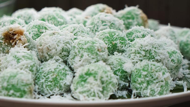 Indonesische Klepon werden mit Kokosraspeln bestreut und auf Bananenblättern serviert.