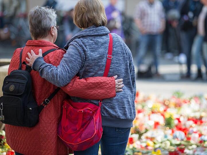 Zwei Trauernde Personen stehen vor einem Meer von Trauerkerzen und Blumen am Tatort, der Münsteraner Gaststätte "Großer Kiepenkerl".