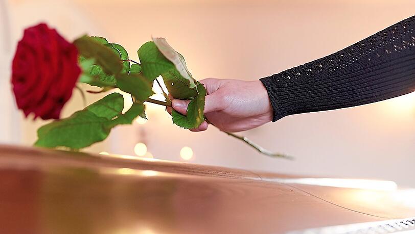 Eine Frau legt eine Rose auf einen Sarg. Eine Frau legt eine Rose auf einen Sarg.