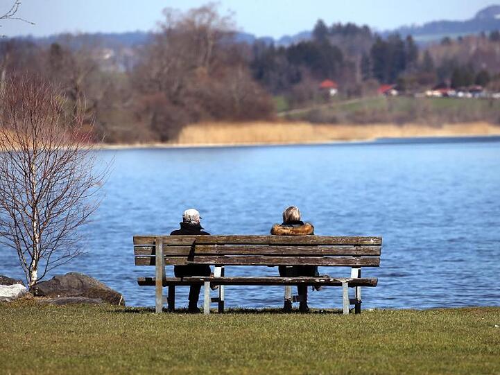 Ausflügler genießen auf einer Bank am Niedersonthofener See den Sonnenschein. Foto: Karl-Josef Hildenbrand/dpa/Archivbild