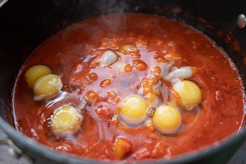 Sobald das Gem&uuml;se weich ist, geben Sie die restlichen Zutaten in die Pfanne: einen Essl&ouml;ffel Tomatenmark, etwas Kreuzk&uuml;mmel, Paprika, Zimt, einen halben Bund gehackte Petersilie sowie Salz und Pfeffer. Alles f&uuml;r rund 35 Minuten k&ouml;cheln lassen. Anschlie&szlig;end mit einem L&ouml;ffelr&uuml;cken kleine Mulden in die So&szlig;e dr&uuml;cken und jeweils ein Ei hineinschlagen.