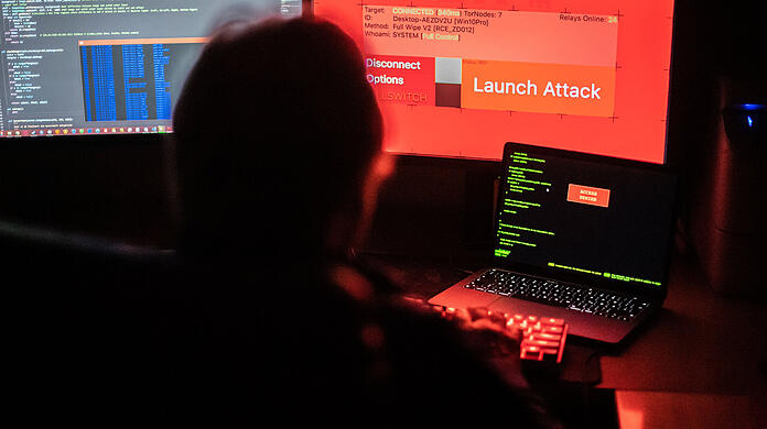Ein Mann sitzt vor Bildschirmen, die Hacker-Programme und eine fiktive Fernlösch-Software zeigen. (Symbolbild)