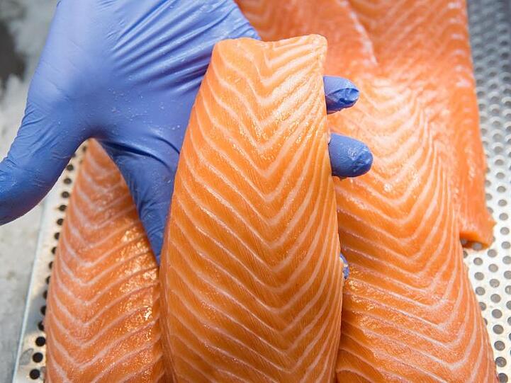 Ein Mitarbeiter präsentiert in einem Fischmarkt in einer Kühlvitrine liegenden Lachs.