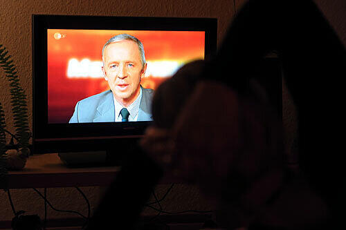 Eine Passantin verfolgt an einem Bildschirm den TV-Auftritt von Christoph Koch
