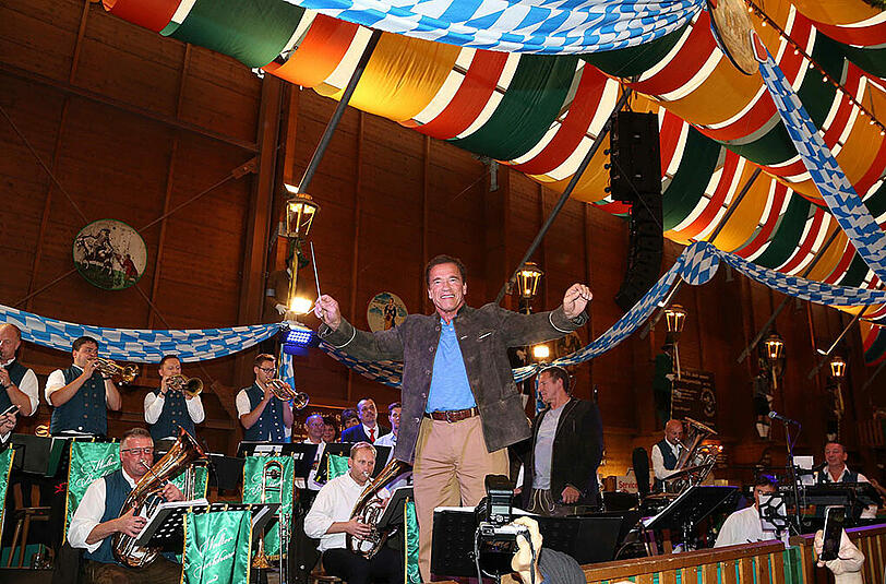 Arnold Schwarzenegger dirigiert im Schützenzelt das Wiesn-Volk.
