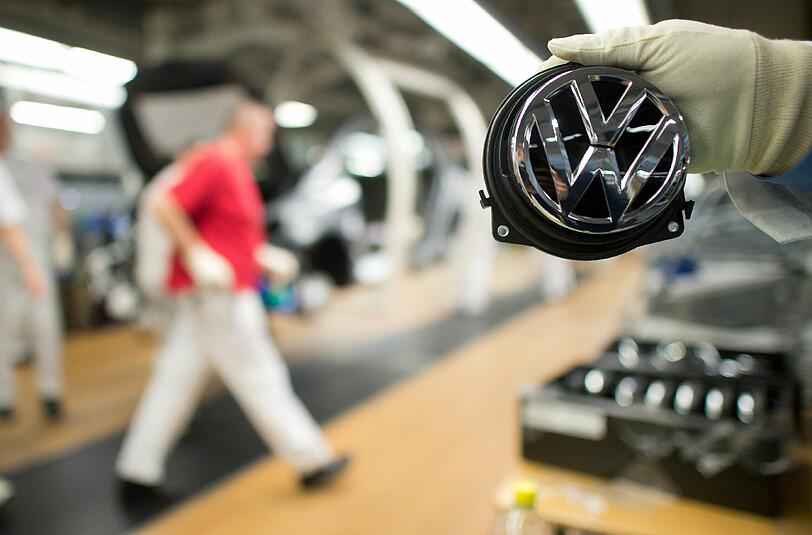 Ein Mitarbeiter zeigt in Wolfsburg ein Volkswagen-Logo. Foto: Foto: Julian Stratenschulte