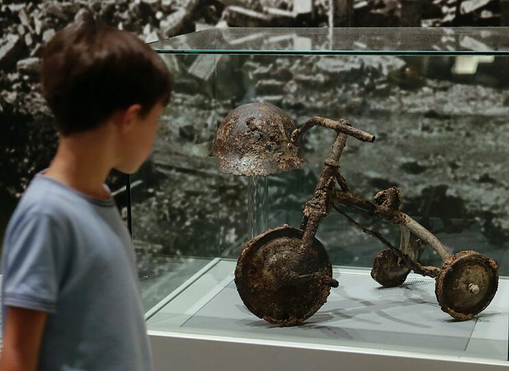 Ein Bub blickt im &bdquo;Hiroshima Peace Museum&ldquo; auf ein Dreirad und einen Helm. Sie gehörten dem dreijährigen Shinichi, der 1945 verglühte.
