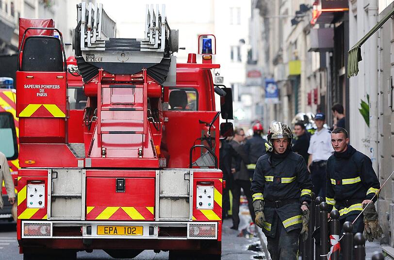 Feuerwehrmänner stehen in der Straße in Paris, in der es in einem Parkhaus eine schwere Explosion gegeben hatte.