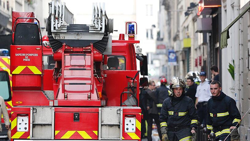 Feuerwehrmänner stehen in der Straße in Paris, in der es in einem Parkhaus eine schwere Explosion gegeben hatte. Feuerwehrmänner stehen in der Straße in Paris, in der es in einem Parkhaus eine schwere Explosion gegeben hatte.