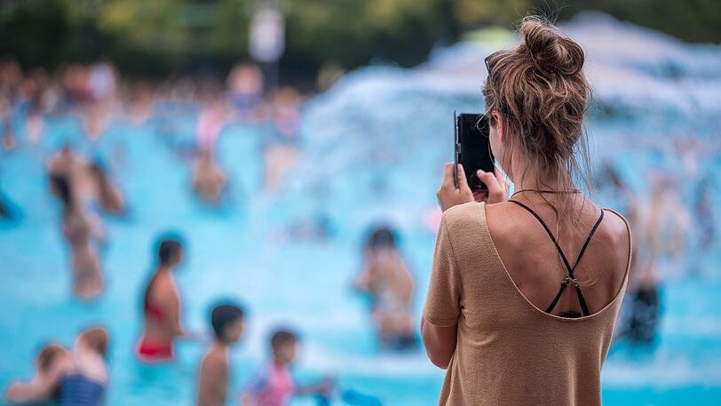 Eine junge Frau fotografiert mit ihrem Handy im Prinzenbad. Mama, Papa und die Handykamera sind immer dabei.