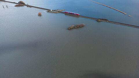 Ein Personenzug der Deutschen Bahn fährt im Januar 2023 durch eine überschwemmte Flussniederung bei Eichen in Hessen.