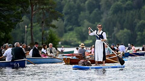 Ein Frau im Dirndl nimmt auf einem Stand-Up Board an der Seeprozession zu Fronleichnam auf dem Staffelsee teil.