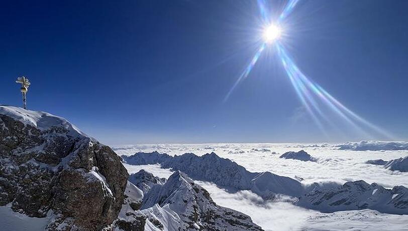 Die Sonne scheint über dem Gipfelkreuz der schneebedeckten Zugspitze.
