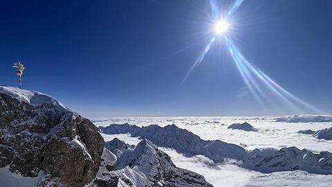 Die Sonne scheint über dem Gipfelkreuz der schneebedeckten Zugspitze.