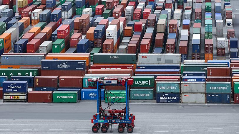Ein Van-Carrier (VC) fährt über den Container-Lagerplatz am Containerterminal Burchardkai im Hafen an einer Reihe gestapelter Container vorbei. (Symbolbild)
