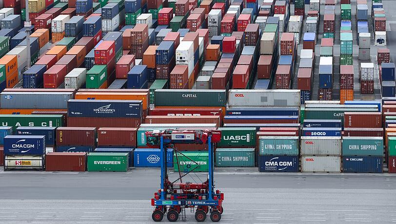 Ein Van-Carrier (VC) fährt über den Container-Lagerplatz am Containerterminal Burchardkai im Hafen an einer Reihe gestapelter Container vorbei. (Symbolbild) Ein Van-Carrier (VC) fährt über den Container-Lagerplatz am Containerterminal Burchardkai im Hafen an einer Reihe gestapelter Container vorbei. (Symbolbild)