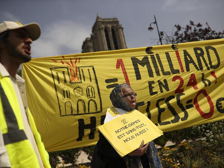 Bei einem Protest am Ostermontag vor der Notre-Dame Kathedrale werden Banner mit der Aufschrift auf Französisch: "Eine Milliarde in 24 Stunden! Obdachlos Null" und "Notre-Dame ist dachlos, wir auch!" gezeigt.