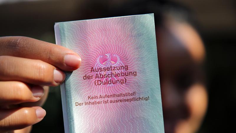 Eine junge Frau hält einen Ausweis für Flüchtlinge in der Hand mit dem Titel: Aussetzung der Abschiebung (Duldung). Eine junge Frau hält einen Ausweis für Flüchtlinge in der Hand mit dem Titel: Aussetzung der Abschiebung (Duldung).