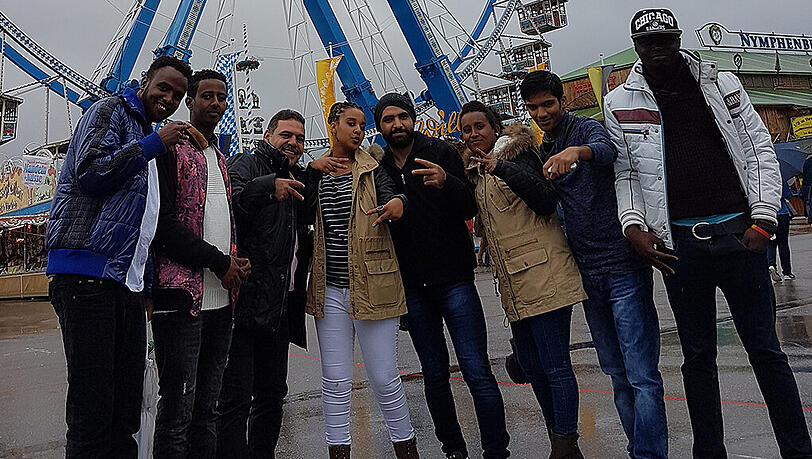 Die Gruppe Geflüchteter posiert für ein Erinnerungsfoto vor dem Riesenrad. Die Gruppe Geflüchteter posiert für ein Erinnerungsfoto vor dem Riesenrad.