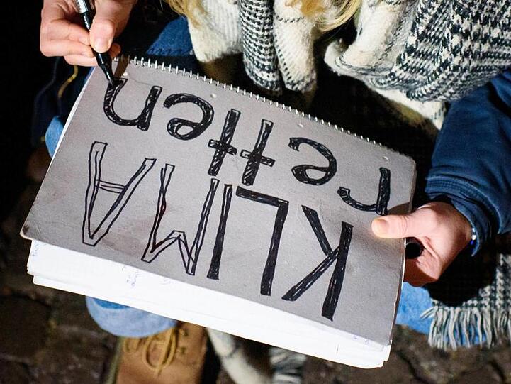 Eine Gegnerin des Braunkohlenbergbaus malt ein Schild mit der Aufschrift "Klima Retten". Foto: Gregor Fischer/Archivbild