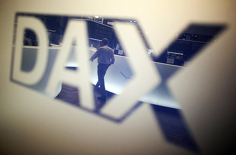 Ein Händler geht über das Parkett in der Börse in Frankfurt am Main und spiegelt sich dabei in einem Logo des Deutschen Aktienindexes (DAX). Foto: Fredrik von Erichsen