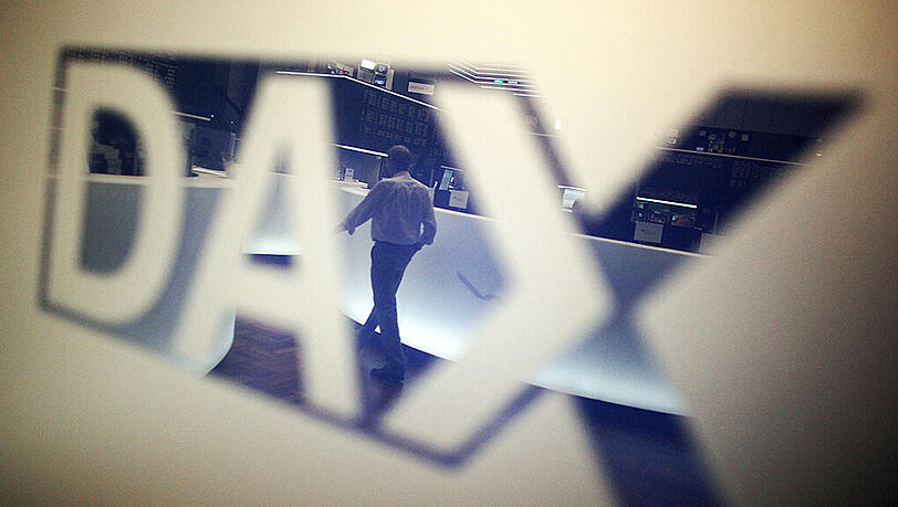 Ein Händler geht über das Parkett in der Börse in Frankfurt am Main und spiegelt sich dabei in einem Logo des Deutschen Aktienindexes (DAX). Foto: Fredrik von Erichsen