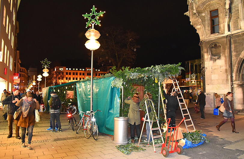 Ein Budenbetreiber befestigt Tannenzweige an seinem Stand.