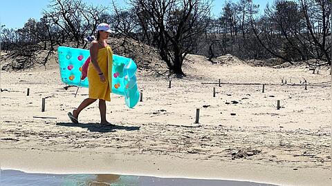 Eine Touristin am Strand von Rhodos vor verbrannter Natur.