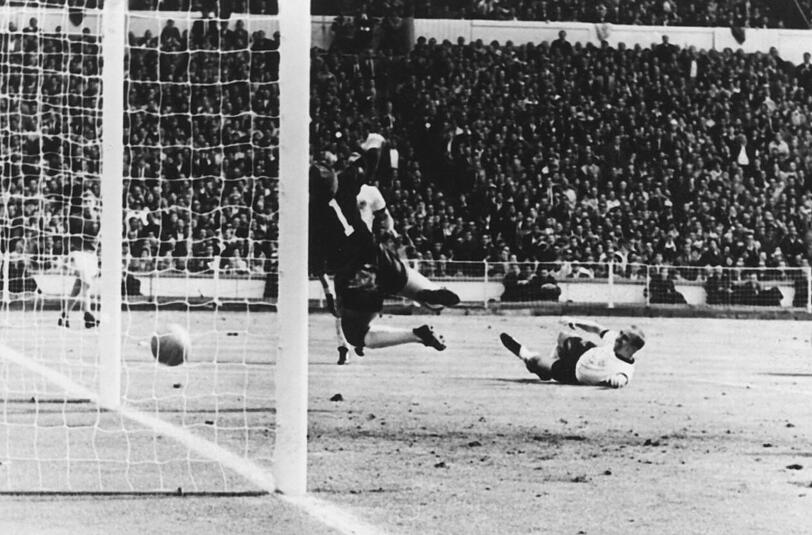 Der englische Stürmer Geoff Hurst (r) knallt den Ball unter die Latte, der deutsche Torhüter Hans Tilkowski (l) kommt nicht an das Leder, dem der deutsche Abwehrspieler Willi Schulz (M) bei seinem Flug nachschaut. Es wird nach Befragen des russischen Linienrichters schließlich auf Tor entschieden. England geht mit 3:2 in Führung und gewinnt am Ende mit 4:2 und damit den Weltmeistertitel.