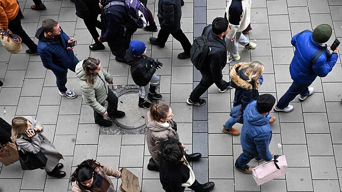 Männer und Frauen mit Einkaufstüten gehen durch die Fußgängerzone der Einkaufsmeile.