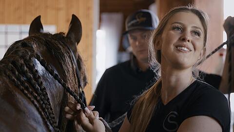 Die Doku "Pferdest&auml;rke - Die Welt der Gina Schumacher" begleitet die Tochter von Michael Schumacher in ihrem Alltag, der stark von ihrer Leidenschaft f&uuml;r Pferde und Reiten gepr&auml;gt ist. Im Hintergrund ist ihr Ehemann Iain Bethke zu sehen.