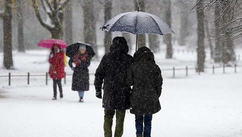 Eine Mann und eine Frau spazieren mit einem Regenschirm bei leichtem Schneefall durch den Englischen Garten.