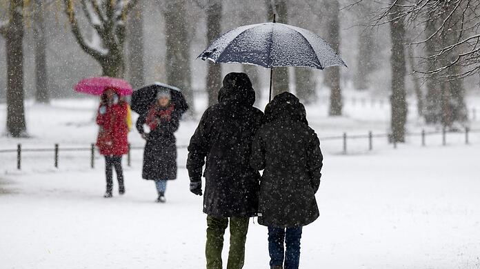 Eine Mann und eine Frau spazieren mit einem Regenschirm bei leichtem Schneefall durch den Englischen Garten.